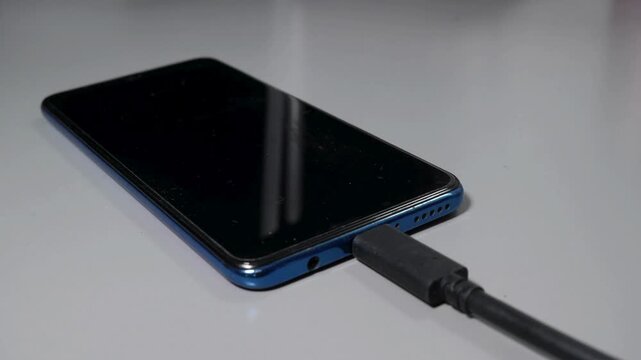 hand plugging the charger into mobile cell phone usb c data cable connecting to charging plug socket.