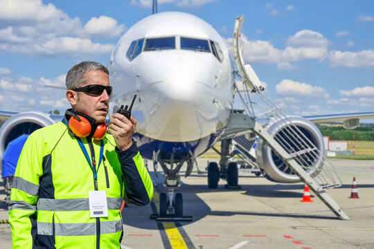 Airport ground crew worker coordinating operations with walkie-talkie during aircraft ground handling on ramp.