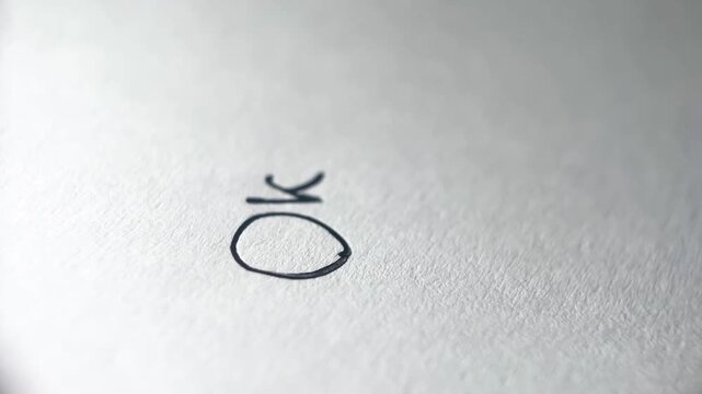 Close-up of pen tip writing OK on white paper with blurred finger in background