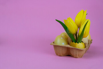 Obraz premium Easter greeting card with yellow tulips in eggshell and decorated eggs in carton on pastel background with copy space