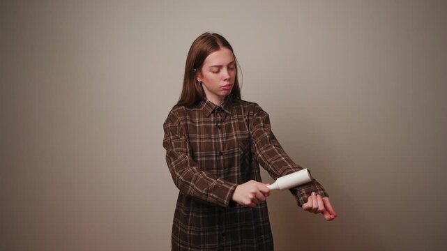 Woman using lint roller to clean brown plaid shirt, clothing care routine.