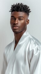 Obraz premium Young Black Man with Curly Hair Wearing a White Silk Robe, Looking Confidently