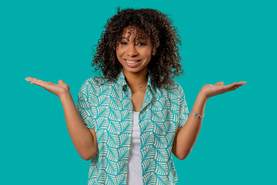 Pretty young woman, shoulders up - cant help, makes gesture of I dont know. Difficult question, guilty reaction, on blue background.