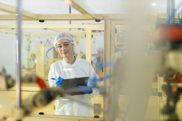 Obraz premium Quality control technician in food processing factory recording inspection data on clipboard. Focus on hygiene, safety standards, and compliance in industrial manufacturing.
