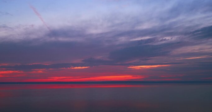 The sun shines through the clouds on a sunset. Blue sky with clouds. A calm river against the backdrop of a vibrant sunset. Time-lapse photography.