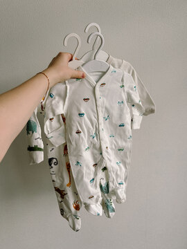Woman holds set of sleepsuits for newborns made of cotton with buttons on hangers. Vertical