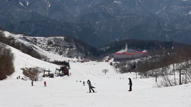 Wide view of people enjoying winter sports on a snowy mountain ski run on a clear day