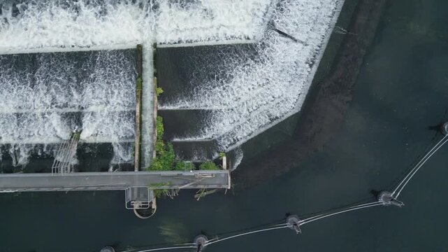 Aerial view of a cascading waterfall and a footbridge over dark water.