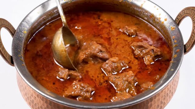 Close-up of stirring spicy Mutton Rogan Josh in a copper bowl. Traditional Indian meat curry with rich red gravy. Authentic cuisine concept