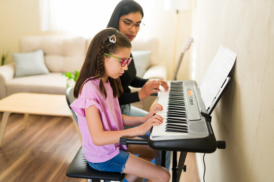 Young girl learning piano with female music teacher helping hands during private lesson at home
