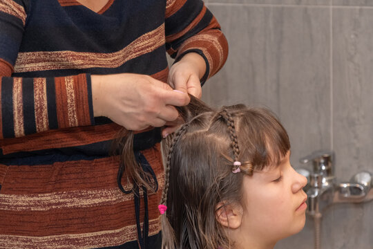 Woman's hands carefully interlace strands of girl's hair creating neat hairstyle after washing.