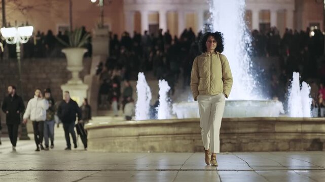 Stylish tourist woman strolls through a lively Athens city Syntagma square at night, slow motion
