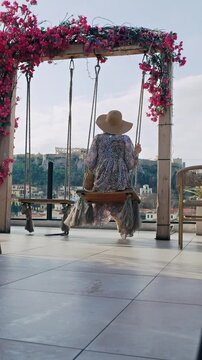 Woman on swing with panoramic view of Athens skyline and ancient Acropolis temple