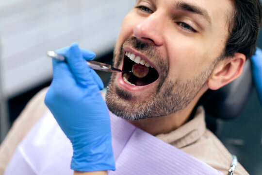 Man patient sitting in dental chair while dentist examining his teeth using dental tools, male receiving dental checkup and treatment