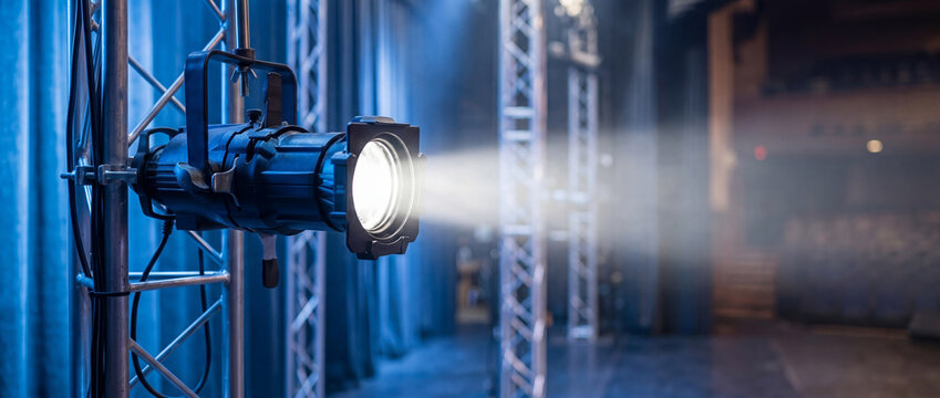 Professional stage spotlight on a metal truss in a theater. Bright white light beam with haze and blue atmospheric background lighting. Backstage event production and theatrical equipment scene