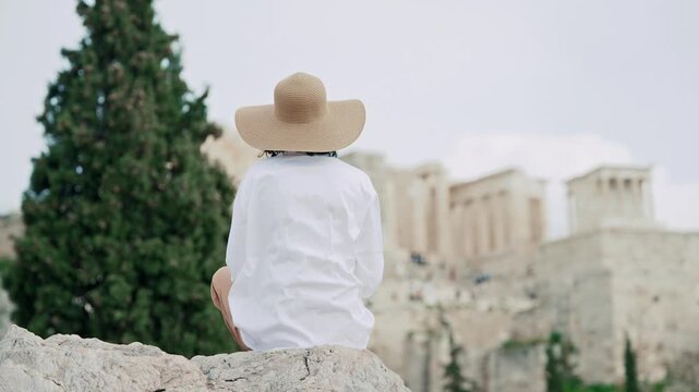 Woman seated on rock facing the Acropolis in Athens, Greece