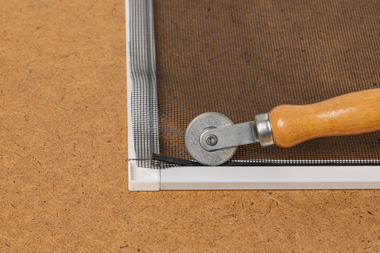 Repairing window screen frame with new fiberglass mesh. Home repair, maintenance, and insect control concept.