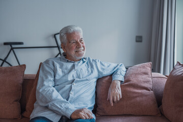 Fototapeta premium Older man relaxing on sofa at home, smiling senior enjoying a quiet afternoon and domestic comfort