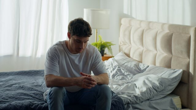 Caucasian man sitting on bed at home holding head grief pain depressed male exhausted guy crisis separation headache burnout mental health sadness anxiety distraught overworked loss indoors bedroom