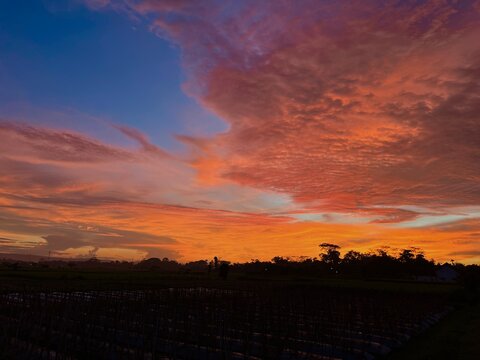 Vibrant orange and purple twilight sky filled with colorful clouds above rural landscape silhouette