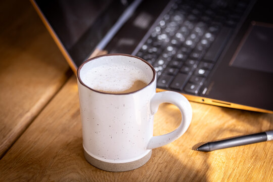 Frischer Kaffee mit etwas Milchschaum, im Hintergrund ist ein Laptop und ein Stift zu sehen