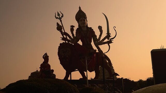 Big Goddess Durga statue at sunset in Chaar Dham Temple in Vrindavan, Uttar Pradesh India. Dramatic spiritual scene, golden sky, temple ambiance, ideal for religion, culture, and festival themes.