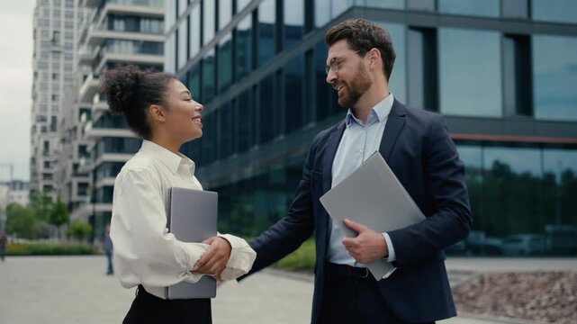 Smiling happy business colleagues hugging meeting in city outside African businesswoman Caucasian businessman friendly greeting partnership coworkers teamwork trust collaboration cheerful conversation