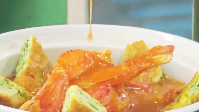Chef pouring spicy and sour shrimp curry with acacia egg omelette, a popular authentic Thai dish.