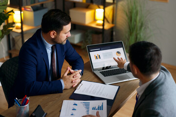 Businessmen discussing financial data points on laptop during meeting