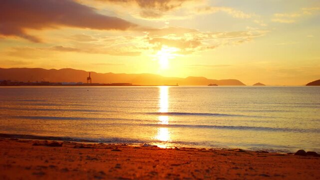 黄金色の夕日が海面を照らす穏やかなビーチの風景