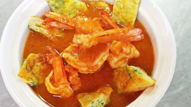 Delicious Thai orange sour curry with prawns and acacia egg omelette in a white bowl.