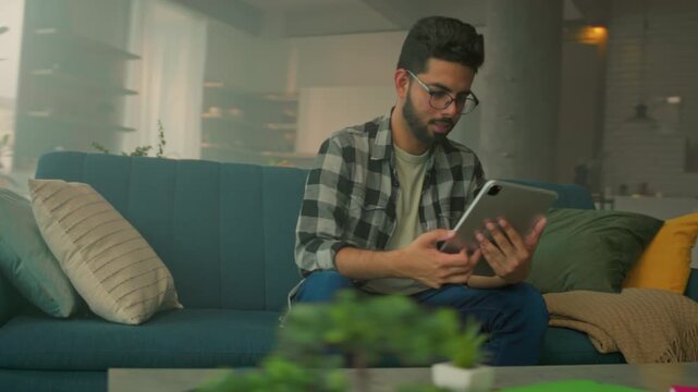 Contemplative individual on cozy sofa, Person relaxing on teal couch surrounded by vibrant artwork and plants
