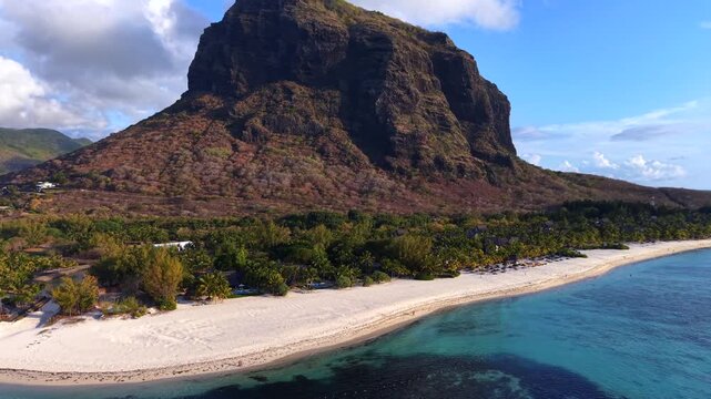 Aerial view of Mount Chamarel's dramatic cliffs. Turquoise waters lap at white sand. Lush greenery lines the coast. Serene beach invites relaxation and escape. Ideal for travel, vacation