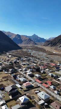 erial cinematic view of Stepantsminda village in Kazbegi, Georgia, surrounded by Caucasus Mountains - Vertical drone shot.