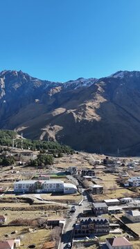 erial cinematic view of Stepantsminda village in Kazbegi, Georgia, surrounded by Caucasus Mountains - Vertical drone shot.