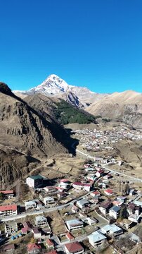 erial cinematic view of Stepantsminda village in Kazbegi, Georgia, surrounded by Caucasus Mountains - Vertical drone shot.