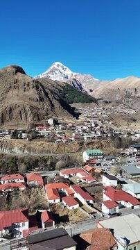 erial cinematic view of Stepantsminda village in Kazbegi, Georgia, surrounded by Caucasus Mountains - Vertical drone shot.