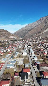 erial cinematic view of Stepantsminda village in Kazbegi, Georgia, surrounded by Caucasus Mountains - Vertical drone shot.