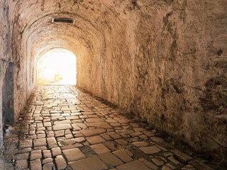 Fototapeta premium Stone tunnel passage inside the Old Fortress in Corfu Old Town, Greece. A bright exit over cobblestone path