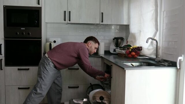 Diligent man rinsing dishes and loading them into the dishwasher at home doing daily chores