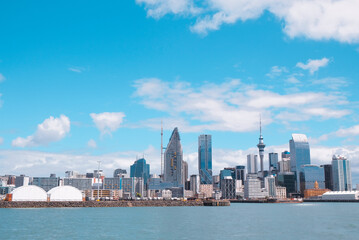 Fototapeta premium Auckland, New Zealand: The city skyline and harbor edge seen from a distance on the water with a wide blue sky overhead