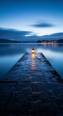 Fototapeta premium Tranquil blue hour scene with a lone lantern illuminating a wet wooden pier extending into a calm lake, reflecting the twilight sky and distant lights.