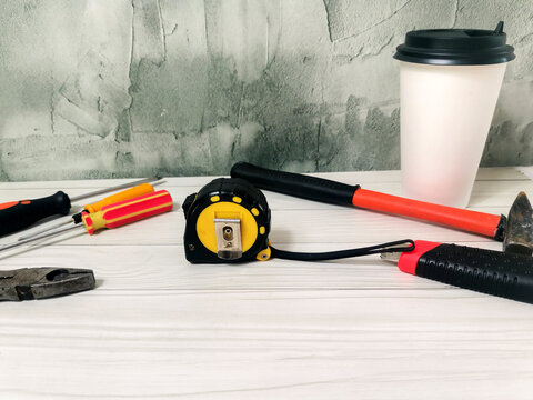 Tools with tape measure, hammer, screwdrivers and coffee on white desk. DIY, repair, handyman workspace