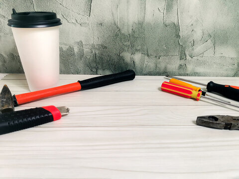 Tools with hammer, screwdrivers, pliers and coffee cup on white wooden desk. DIY repair, handyman workspace, construction, maintenance, home improvement project