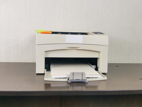 Beige printer with paper on dark wooden desk in home office. Colorful sticky notes on top. Beige textured wall background. Remote work, business documentation, home workspace setup