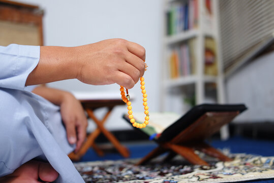 Close-up of hands reciting dhikr using prayer beads with a blurred background. Hands reciting dhikr. A man reciting dhikr while holding a prayer bead. Front view photo

