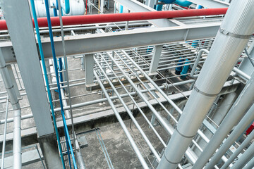 Industrial setting with metal pipes and scaffolding. Red and blue pipes run across gray framework....
