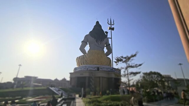 Silhouette of Lord Shiva statue with trishul near a temple during golden sunset in India. Spiritual Hindu scene with devotees, dramatic sky, Chaar Dham Temple in Vrindavan, Uttar Pradesh.