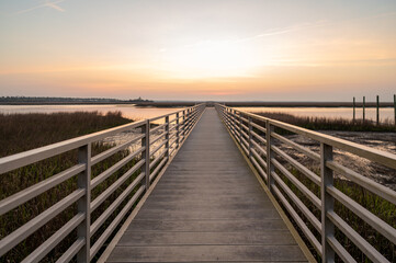 Obraz premium Boardwalk leads to water at sunset near marsh in coastal area