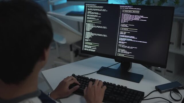 Software developer working on a desktop computer. Programming code running on display. Coding and implementing a technical feature. Specialist typing on keyboard. Working in an agency 